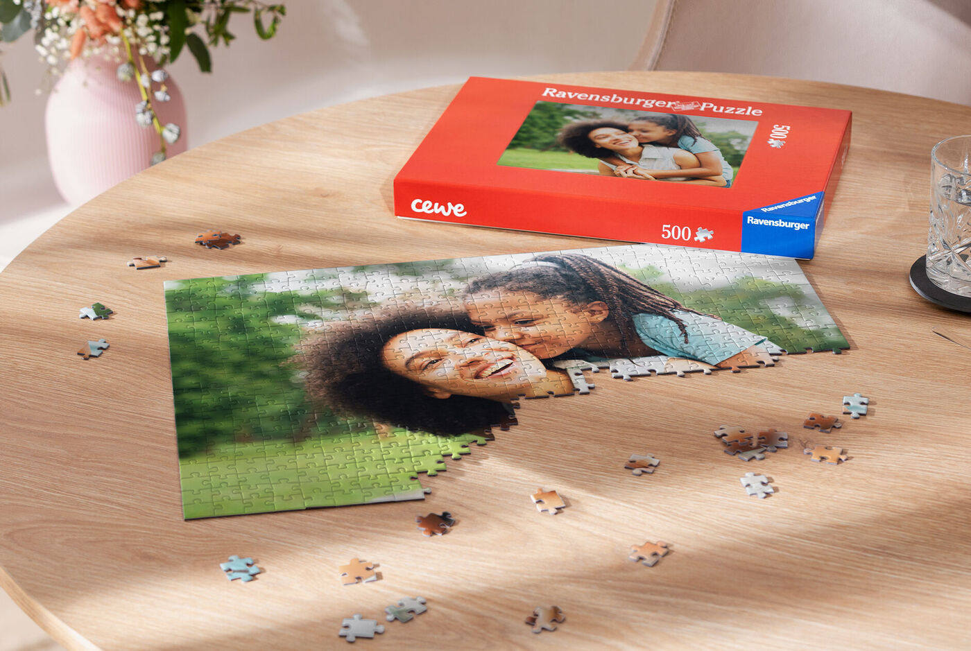 Deux femmes souriantes font un puzzle d'une photo sur une table, à côté se trouve l'emballage du puzzle CEWE Ravensburger