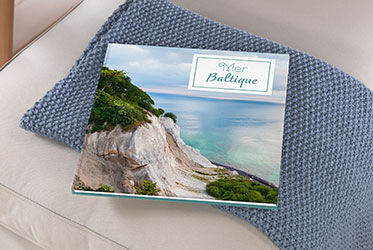 Un magnifique CEWE PHOTOBOOK intitulé "Mer Baltique" repose sur un coussin gris.