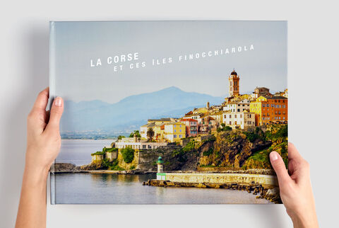 Une personne tient un album photo avec une image de la côte de Corse.