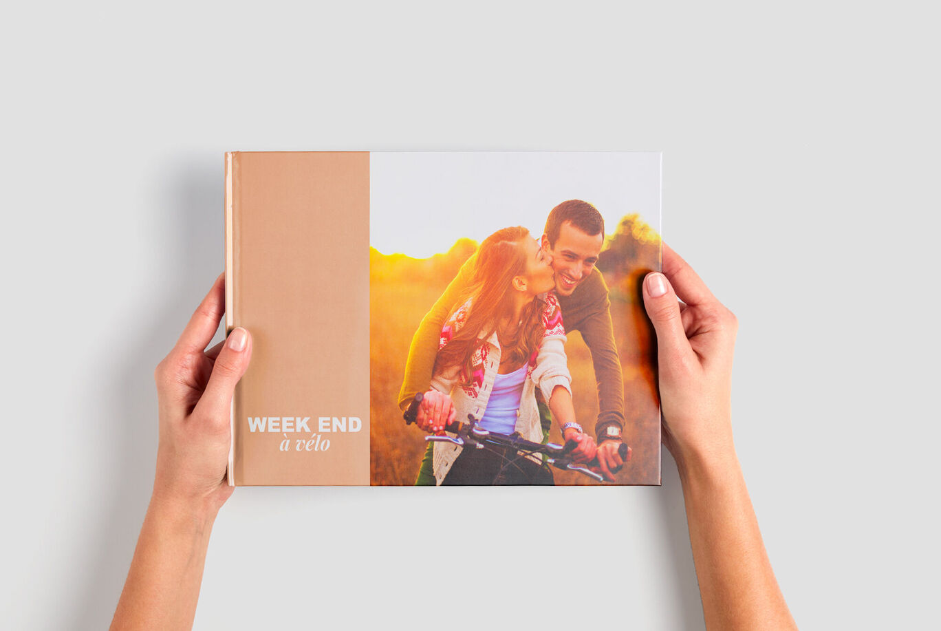 Un couple tient un CEWE Fotobuch devant un beau coucher de soleil