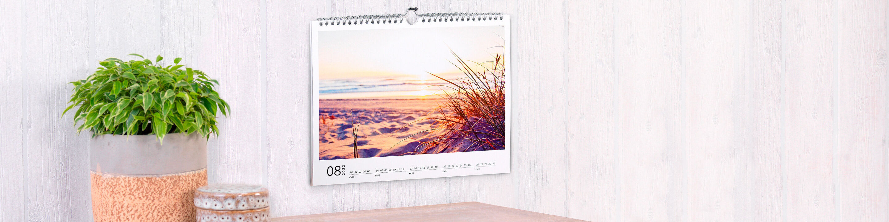 Un joli calendrier photo avec une image de coucher de soleil en août, accroché au mur.
