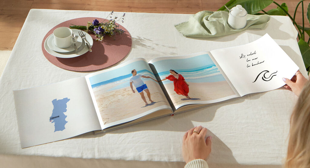 Un couple regarde un livre photo CEWE avec des photos de leurs vacances à la plage.
