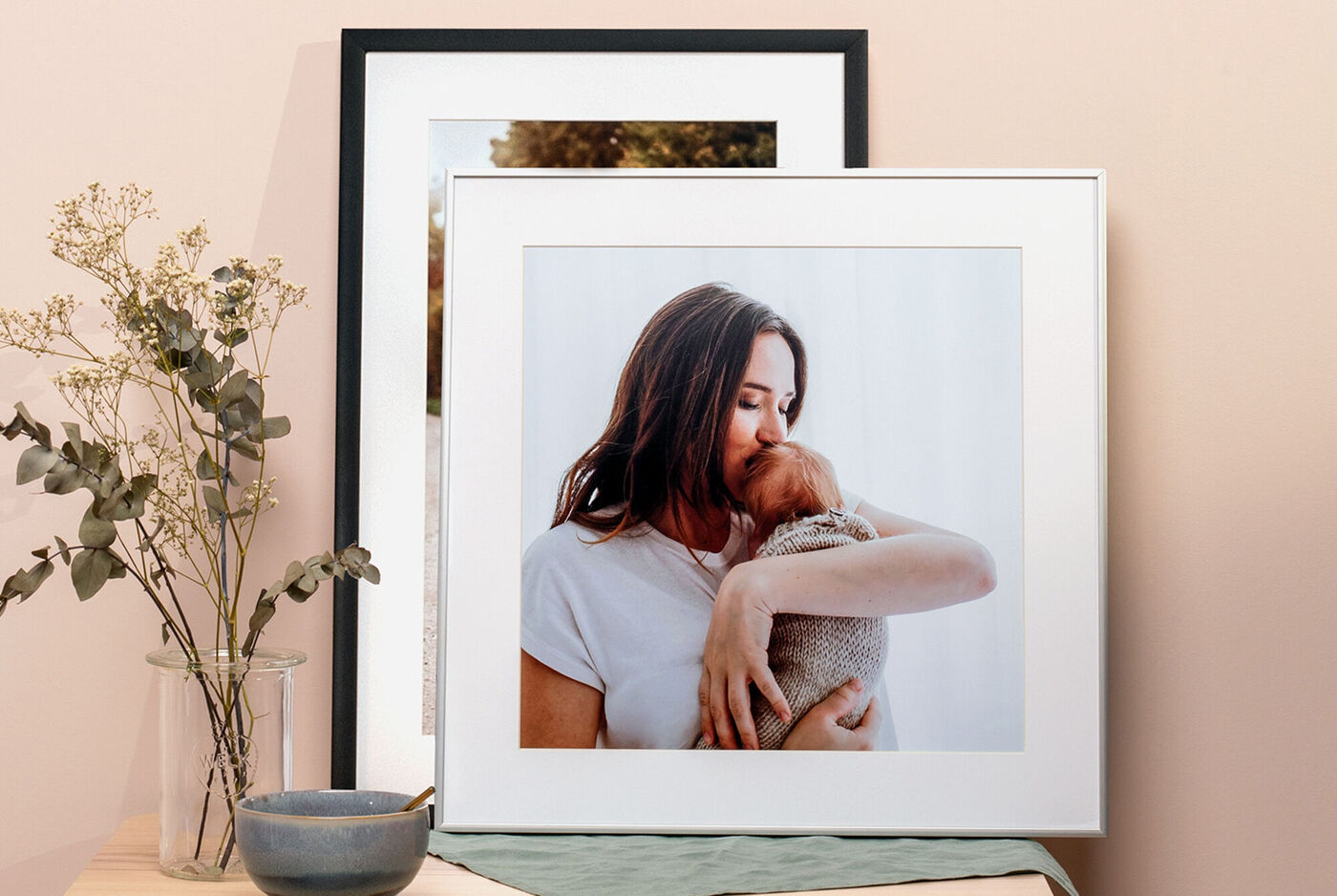 Deux encadrements de poster photo représentant une maman et son bébé, sur une table avec des fleurs séchées