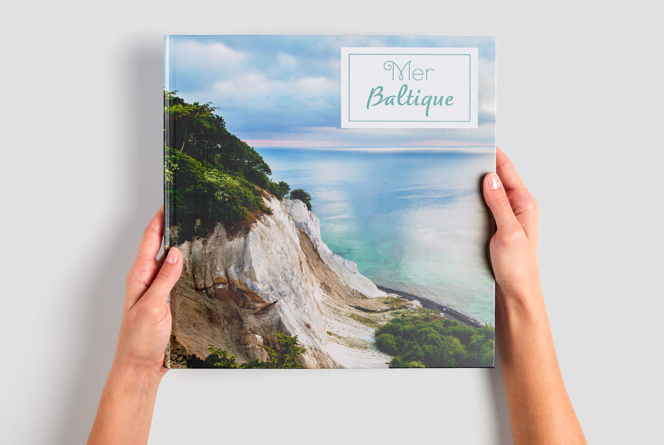 Une personne tient un album photo CEWE avec une image de la mer Baltique.