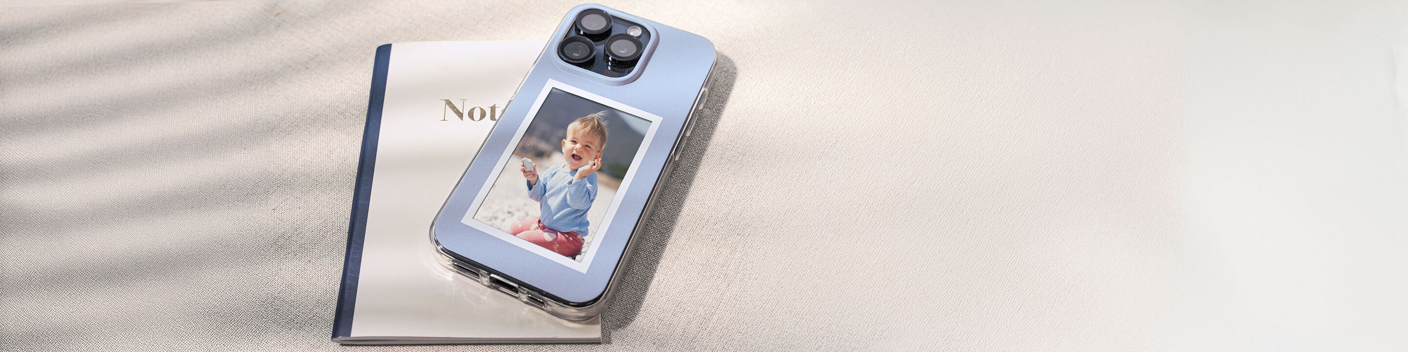 Un smartphone posé sur un carnet. Photo d’un enfant souriant sur l’écran. Arrière-plan doux et lumineux.