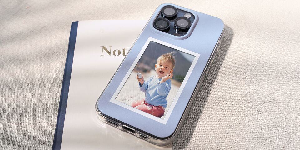 Un téléphone est à côté d'un carnet sur un fond clair. Le téléphone montre une photo d'un enfant.