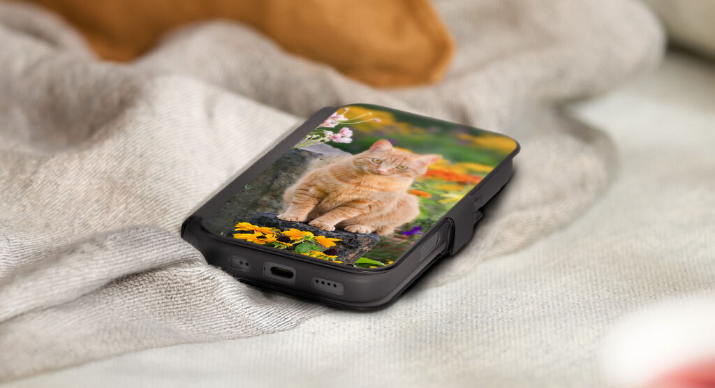 Smartphone posé sur une couverture claire, équipé d’une coque noire personnalisée avec un chaton parmi des fleurs