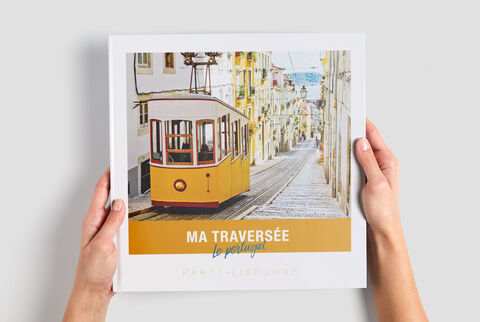 Une personne tient un livre photo CEWE avec une image d'un tramway jaune dans une rue pittoresque.
