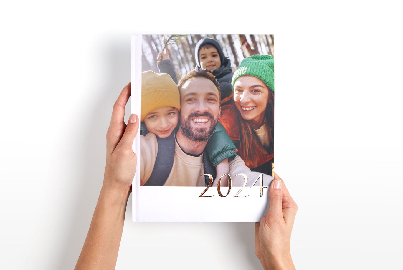 Une personne tient un album photo CEWE avec une couverture colorée et l'année 2024.