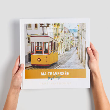 Une personne tient un livre photo CEWE avec un tram jaune dans une ruelle pittoresque au Portugal.