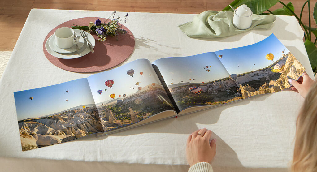 Une personne feuillette un livre photo ouvert avec des ballons et des paysages en arrière-plan